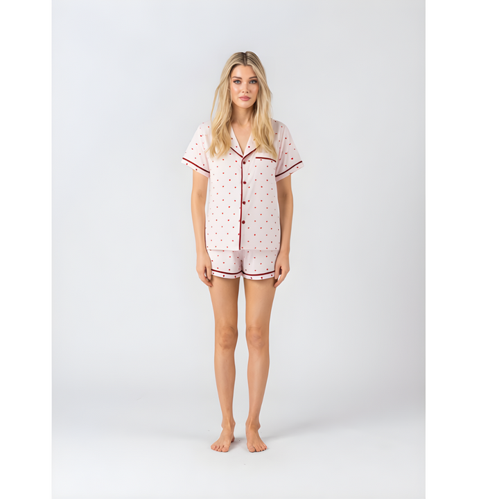 Woman wearing light pink short-sleeve pyjamas with red heart print and red piping trim.