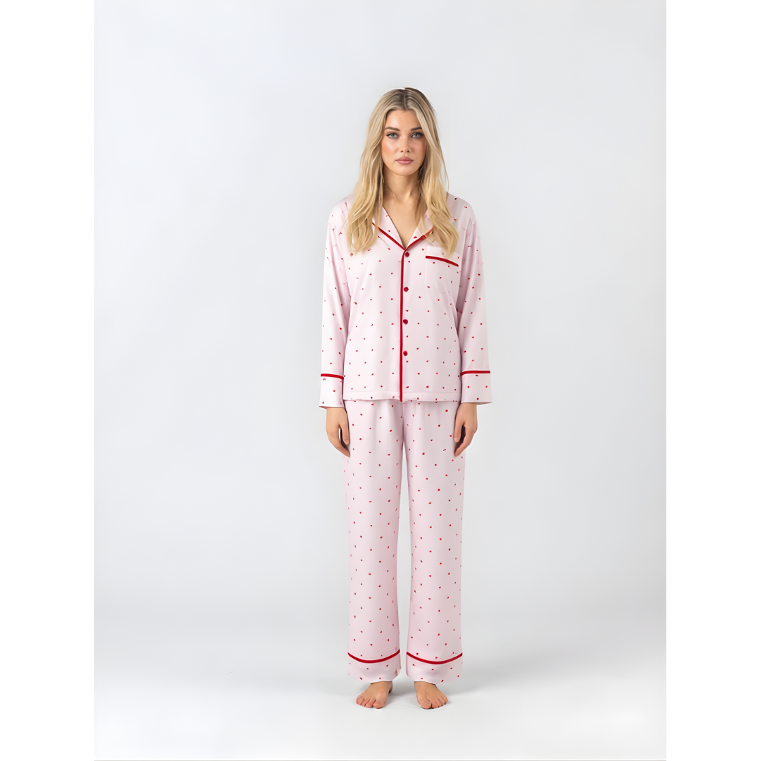 Model wearing a full-length pink pyjama set with small red hearts and red contrast piping.